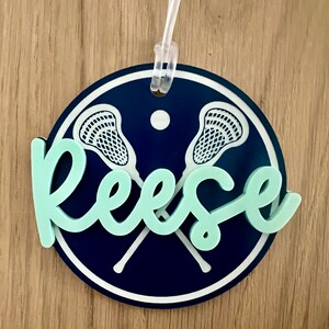 May include: A round, blue and white lacrosse themed luggage tag with the name "Reese" in light green.