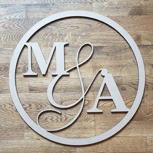 May include: A wooden circle with the letters "M & A" cut out in a cursive font. The circle is on a wood background.