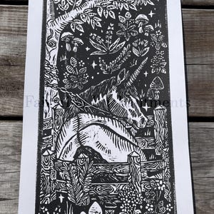 May include: Black and white linocut print featuring a unicorn in a forest setting. The artwork includes a detailed depiction of trees, foliage, mushrooms, and a wooden fence. The print has the text "Fairyring Enchantments" at the top and bottom.