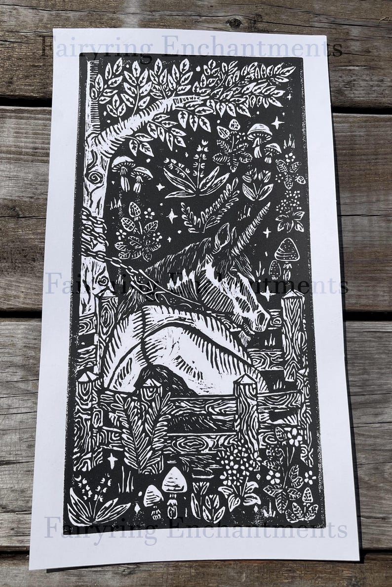 May include: Black and white linocut print featuring a unicorn in a forest setting. The artwork includes a detailed depiction of trees, foliage, mushrooms, and a wooden fence. The print has the text "Fairyring Enchantments" at the top and bottom.