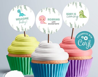 Könnte beinhalten: Drei Cupcakes mit grünen, blauen und violetten Cupcake-Förmchen. Jeder Cupcake hat einen anderen Dinosaurier-Topper mit dem Text "Willkommen Baby!", "Brüllend vor Aufregung!" und "Baby kommt".