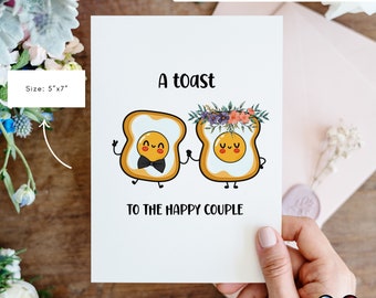 May include: A printable wedding card with a toast to the happy couple. The card features two cartoon pieces of toast with fried eggs and faces. One toast has a bow tie and the other has a floral crown.