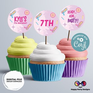 May include: Three pink and white cupcake toppers with a pink background and images of toy guns and targets. The toppers say "Kyle's 7th Birthday!" "7th" and "Ready... Aim... Party!"