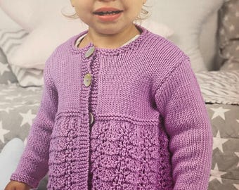 May include: A little girl wearing a purple knitted cardigan with a button closure and a scalloped hem. She is wearing a pink dress with white hearts and a gray headband.