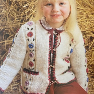 May include: A white knitted cardigan with a floral design, featuring red, blue, and purple accents. The cardigan has a crocheted trim and a tie closure.