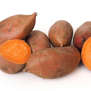 May include: A group of six sweet potatoes, some whole and some cut in half, showing the orange flesh inside. The potatoes are arranged on a white surface.