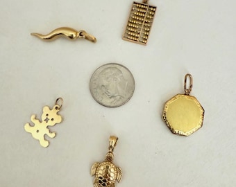 Könnte beinhalten: Eine Sammlung goldfarbener Anhänger, darunter ein Horn, ein Abakus, ein Teddybär, eine Schildkröte und ein achteckiges Medaillon. Eine Münze dient zum Größenvergleich. Die Anhänger sind wahrscheinlich für Halsketten oder Armbänder.