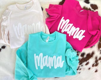 May include: Three sweatshirts with the word "Mama" printed in white on each. The sweatshirts are in different colors: cream, pink, and turquoise.