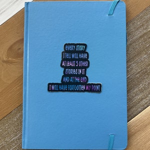 Puede incluir: Un cuaderno azul con una pegatina que dice "Cada historia que cuento tendr&aacute; al menos 5 historias m&aacute;s en ella y al final me habr&eacute; olvidado de mi punto."