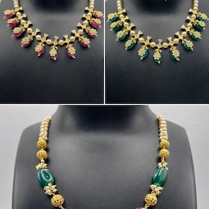 May include: A collection of three necklaces and earrings sets. The sets feature gold-colored metal, pearls, and gemstones in shades of red, green, and gold. The jewelry is displayed on black mannequins.