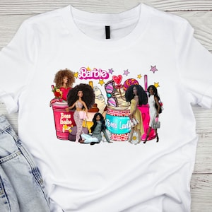 May include: White t-shirt featuring a colorful graphic with the word "Barbie" and several dolls. The graphic includes the words "Boss babe" and "Boss Lady" with pink and purple accents.