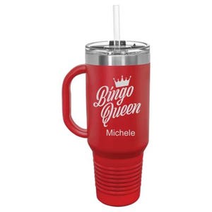 May include: Red stainless steel travel mug with a handle and a straw. It has a white design that says "Bingo Queen" with a crown above the word "Bingo". The name "Michele" is printed below the design.