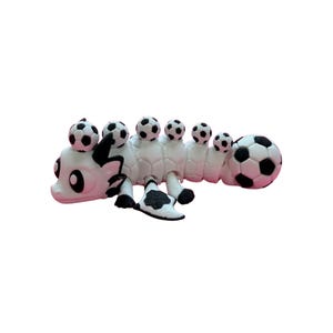 May include: A whimsical white and black caterpillar-like sculpture with soccer balls on its back and at the end. The sculpture has a cartoonish design with a playful aesthetic, perfect for sports enthusiasts or as a unique decorative item.