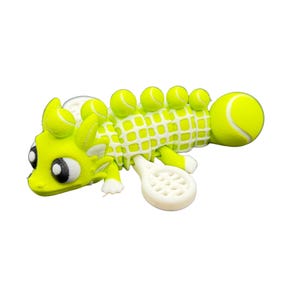 May include: A whimsical, lime green creature with a tennis ball body and head, and a white tennis racket tail. The creature has large black and white eyes and small tennis balls along its back. A fun, unique tennis-themed figurine.