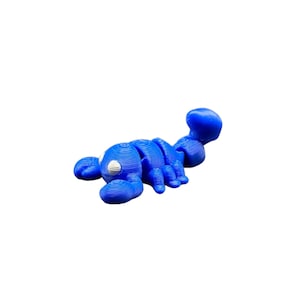 May include: A blue articulated scorpion toy with a segmented body, claws, and a curved tail. The toy has white circular details on its head and is made of a 3D-printed material. The scorpion is lying on a white background.