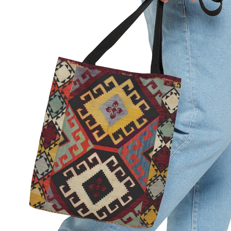 May include: A tote bag with a colorful geometric pattern inspired by traditional rugs. The bag has black straps and a large, rectangular shape.