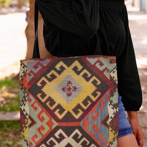 May include: A tote bag with a colorful geometric pattern inspired by traditional rugs. The bag has a black strap and is made of a durable fabric.