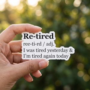 Puede incluir: Una pegatina blanca con el texto "Re-tired" en negrita, en negro. Debajo, la definición "ree-ti-rd / adj." seguida de las frases "I was tired yesterday & I'm tired again today" en negro.
