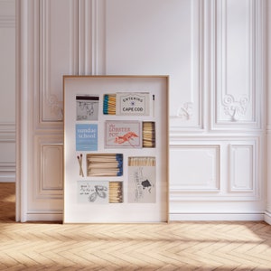 Peut inclure: Un collage encadré de boîtes d'allumettes vintage avec différents motifs, dont "Entering Cape Cod", "The Lobster Pot", "Sundae School" et "Gulls by the Sea". Les boîtes d'allumettes sont disposées en grille et entourées d'une bordure blanche.
