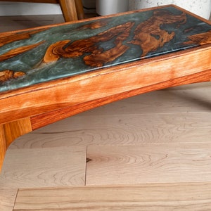 May include: A wooden coffee table with a unique epoxy resin top featuring a swirling blue and brown pattern. The table has a curved, modern design and four legs.