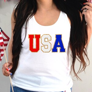 May include: White tank top with the word "USA" in red, white, and blue glitter letters.