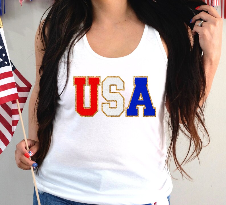 May include: White tank top with the word "USA" in red, white, and blue glitter letters.