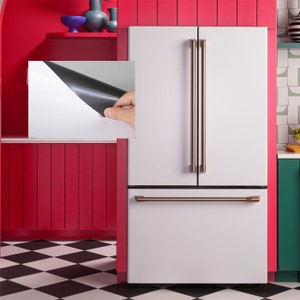 Pode incluir: Um refrigerador branco com acabamento em a&ccedil;o inoxid&aacute;vel e uma al&ccedil;a de n&iacute;quel escovado. O refrigerador tem um design de porta francesa com uma gaveta de congelador inferior.