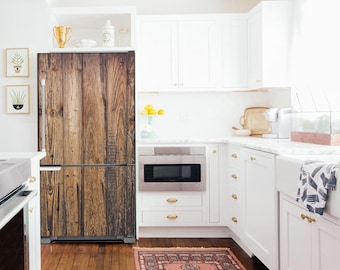 May include: A white kitchen with white cabinets and a stainless steel microwave. The refrigerator has a wood-look door. A rug with a floral pattern is on the floor.