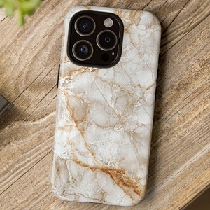 May include: A white and gold marble phone case for an iPhone. The case has a textured surface and a camera cutout.