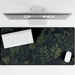 Peut inclure: Un tapis de bureau noir avec un motif de fougères vertes. Un clavier blanc et une souris blanche sont sur le tapis.