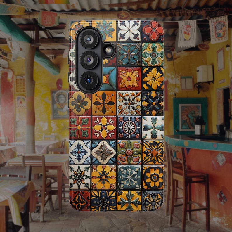 Op de afbeelding: Een rechthoekig telefoonhoesje met een raster van vierkante tegels met diverse bloem- en geometrische patronen in tinten geel, blauw, rood, groen en wit. Het hoesje heeft een verticale camera-uitsparing aan de linkerbovenkant.