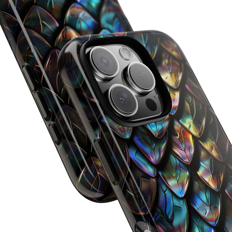 May include: A smartphone case featuring a repeating iridescent dragon scale pattern in shades of deep blue, purple, and gold. The case has a black camera cutout frame and side buttons, showcasing a glossy finish that reflects light across the scales.