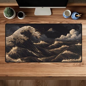 May include: A rectangular desk mat featuring a dark, monochromatic illustration of a large, stylized ocean wave crashing near a mountain peak. The design uses intricate gold and white line work against a deep black background to depict water.