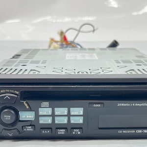 May include: A black Alpine CD receiver, model CDE-7825, with a digital display and various control buttons. The unit has a CD slot and a power button. The text "25 Watts x 4 Amplifier/Regulated 1bit DAC" is visible. Wires extend from the back.