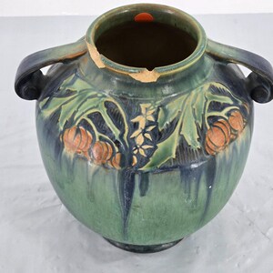 Pode incluir: Um vaso grande de cerâmica verde com duas alças. O vaso apresenta um design floral com detalhes em laranja e verde. O vaso tem uma abertura larga e um corpo arredondado. O vaso tem cerca de 30 cm de altura.