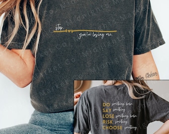 May include: Two black t-shirts with gold text. The front shirt says "stop. you're losing me." The back shirt says "DO something, babe SAY something LOSE something, babe RISK something CHOOSE something".