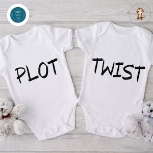 Puede incluir: Dos bodies blancos para bebé con las palabras "PLOT" y "TWIST" impresas en negro. Los bodies tienen mangas cortas y cierres de corchetes. Un osito de peluche blanco está colocado junto a cada body. El fondo es de vetas de madera clara.