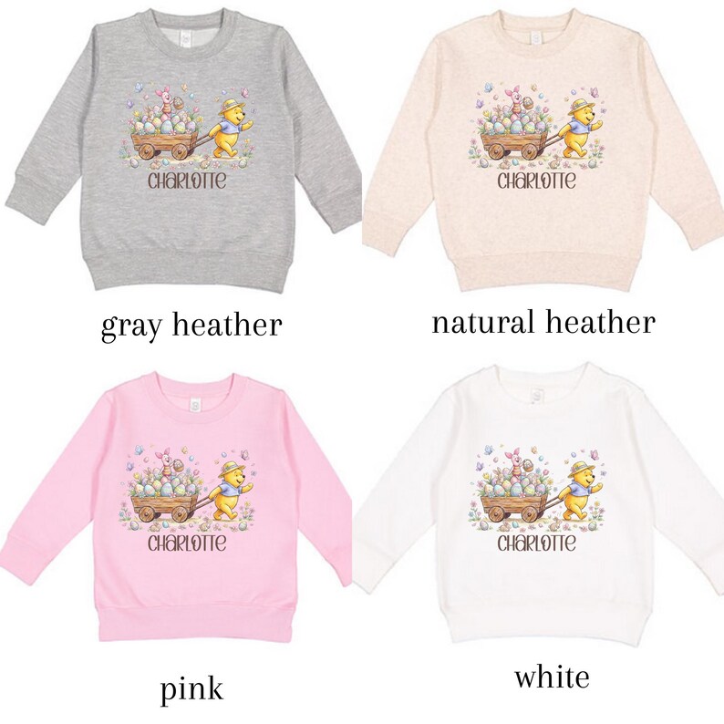 May include: Four children's sweatshirts in gray heather, natural heather, pink, and white. Each features a graphic of a bear pushing a cart filled with Easter eggs, with the name "Charlotte" below. The sweatshirts are long-sleeved.