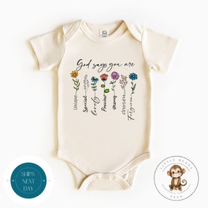 Puede incluir: Un body de bebé de color crema con mangas cortas presenta un diseño floral y el texto "Dios dice que eres" con las palabras "único, especial, adorable, precioso, fuerte, elegido, perdonado" escritas verticalmente junto a cada flor.