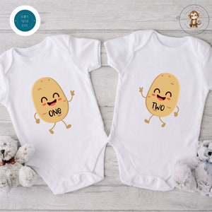May include: Two white baby onesies with a cartoon potato design. The potato on the left onesie has the word "ONE" on it and the potato on the right onesie has the word "TWO" on it.