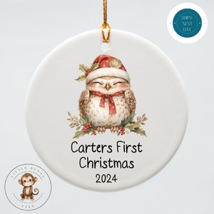 May include: White ceramic Christmas ornament with a cute cartoon owl wearing a Santa hat and a red scarf. The ornament says "Carters First Christmas 2024".