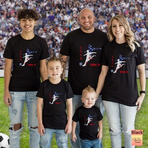 May include: Black t-shirts with a soccer-themed graphic featuring a player silhouette in red, white, and blue, the text "2026 Dallas, TX", and a soccer ball. The shirts are worn by a family of five.