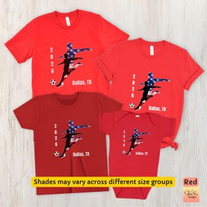 May include: Red t-shirts and a onesie with a soccer player graphic in blue, white, and black. The text "2026 Dallas, TX" is printed on each shirt. The image also includes the text "Shades may vary across different size groups" and "Red".