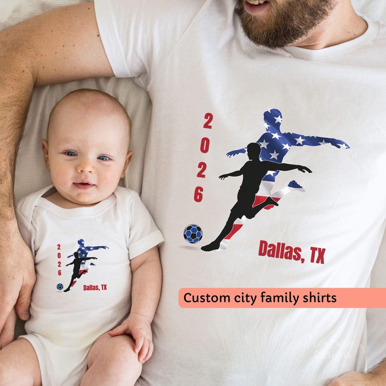 May include: White t-shirts and a onesie with a soccer-themed design. The design includes a soccer player silhouette, the American flag, the year 2026, a soccer ball, and the text "Dallas, TX".