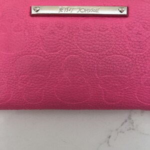 Cartera de pulsera con cremallera en todo el contorno y calaveras en color rosa intenso de Betsey Johnson