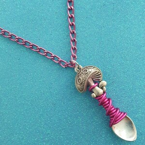 Puede incluir: Un collar de cadena rosa con un dije de cuchara de plata con forma de hongo. La cuchara está envuelta con alambre rosa.