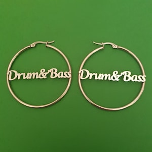 Könnte beinhalten: Ein Paar silberne Creolen mit der Aufschrift "Drum & Bass" auf jeder Creole.