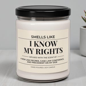 Puede incluir: Una vela de soja blanca en un tarro de cristal con tapa negra. La etiqueta dice "Smells Like I Know My Rights", con texto sobre el aroma. La vela está vertida a mano.