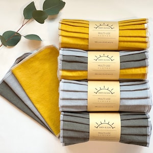 May include: Four sets of multi-use cloths, rolled and stacked. Each set is made of two different colors of fabric, one yellow and one gray. The cloths are labeled "Earth & Son Multi-Use Cloths".