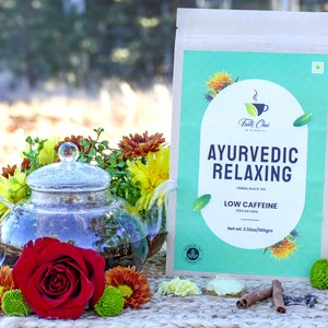 May include: A brown paper bag with a teal and white label that reads "Ayurvedic Relaxing Herbal Black Tea Low Caffeine 100% Natural Net wt. 3.52oz/100gm" with a glass teapot filled with tea and surrounded by flowers and cinnamon sticks.